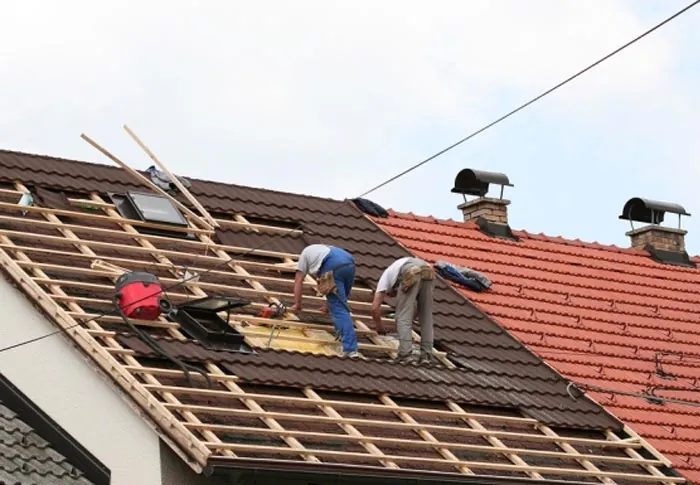 Profissionais instalando telhado cerâmico em obra residencial